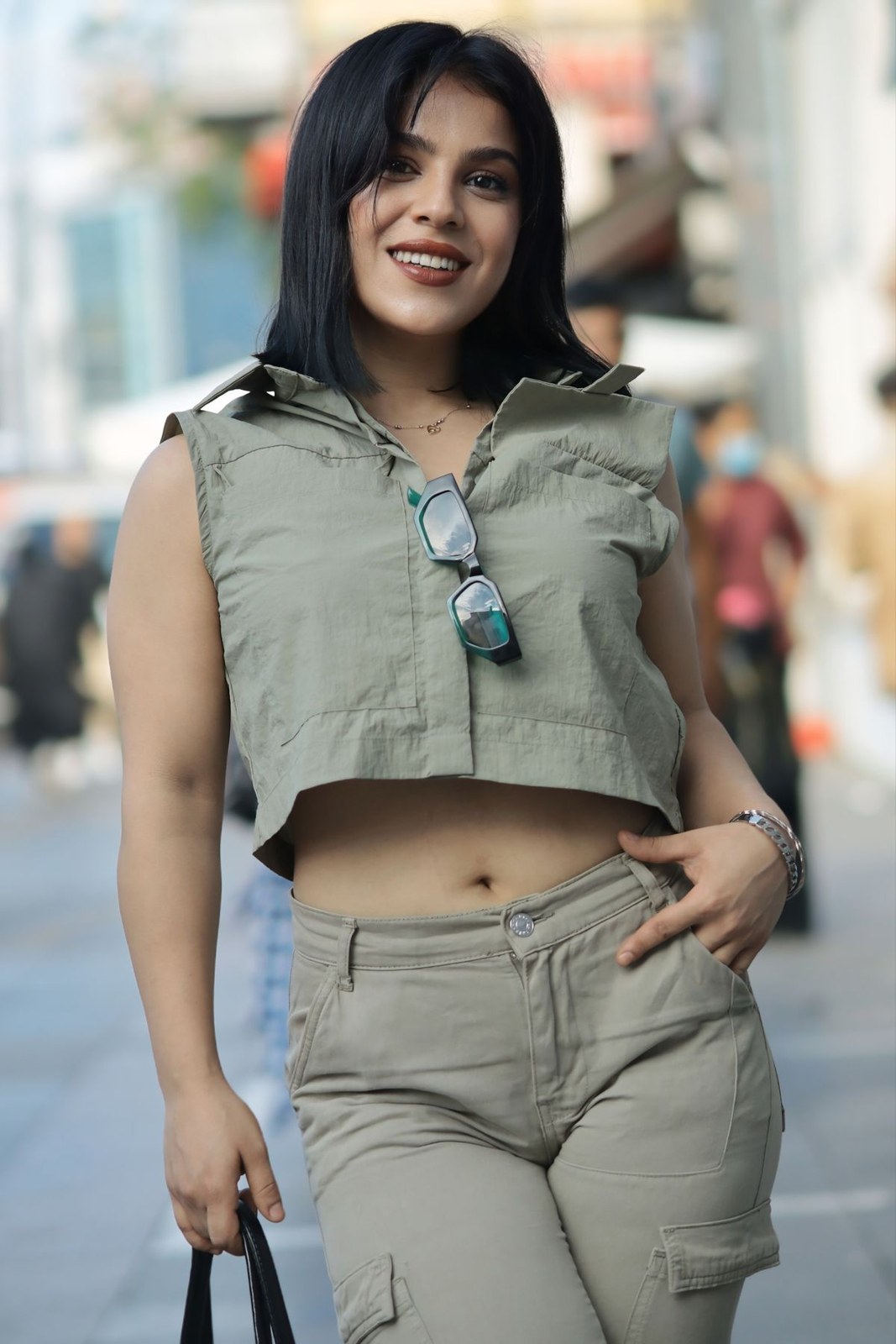 Sage cropped sleeveless hooded top and matching cargo trousers; sunglasses hang at the neckline.