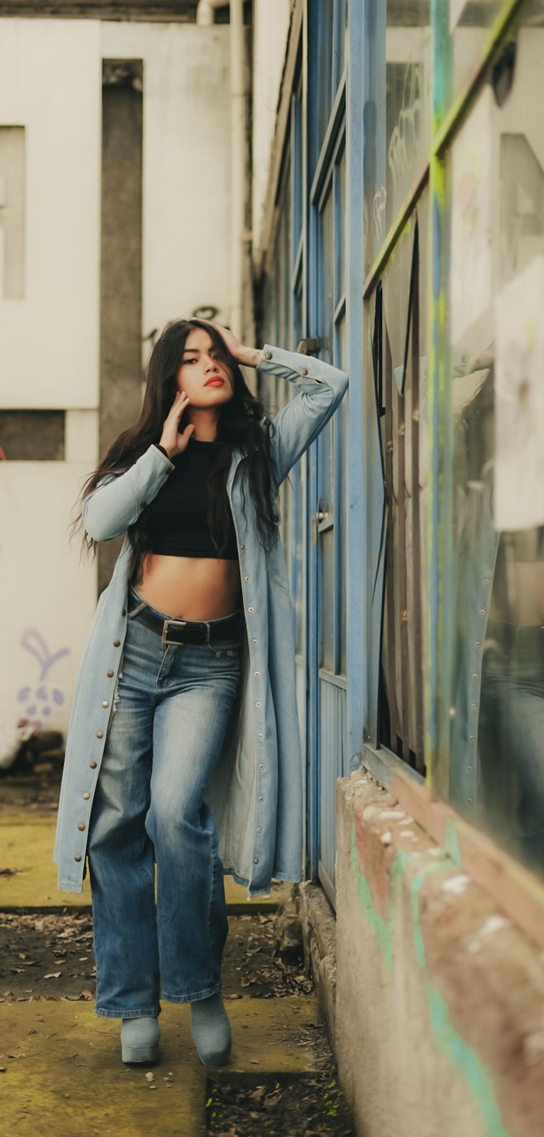 Long pale-blue open layer, black cropped top and loose blue jeans in an alley.