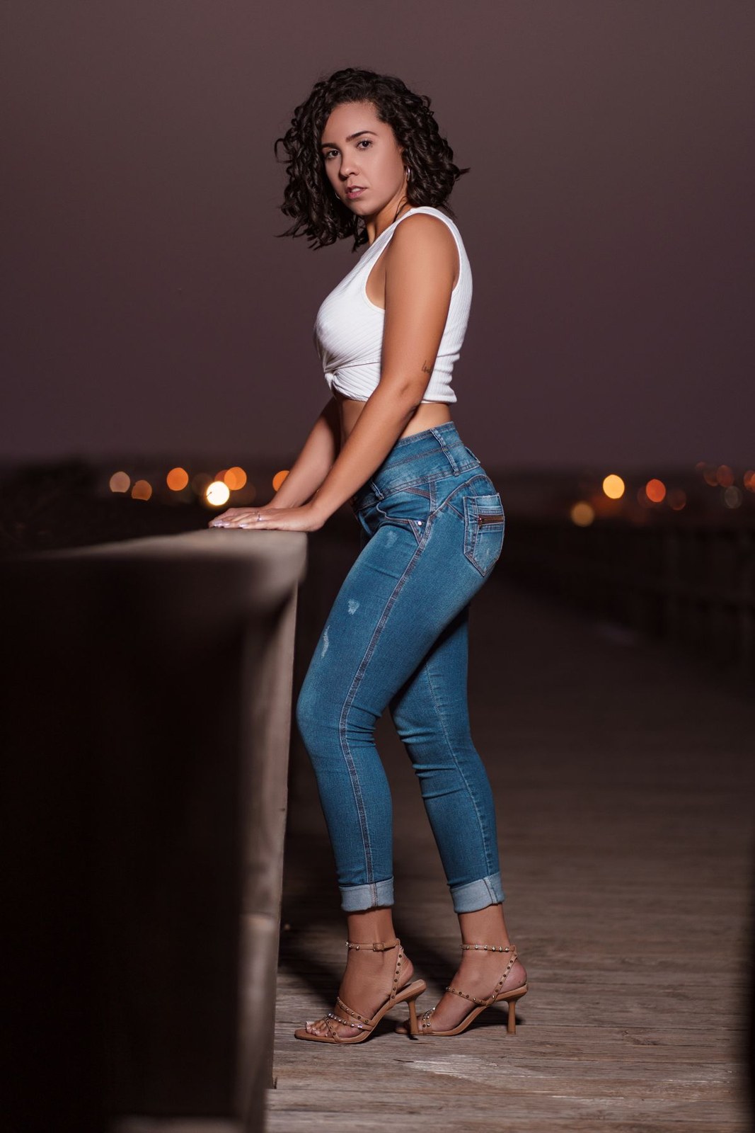 White sleeveless cropped top, cuffed slim blue jeans and pointed high heels at dusk.