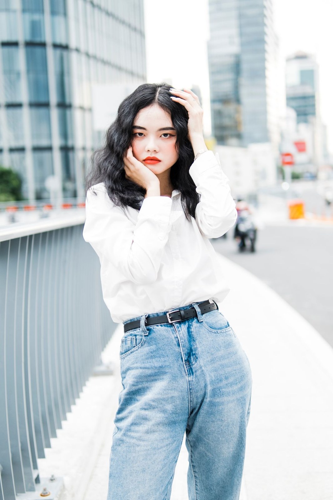 White blouse, pale high-waisted blue jeans and a black belt; upper-body street crop.