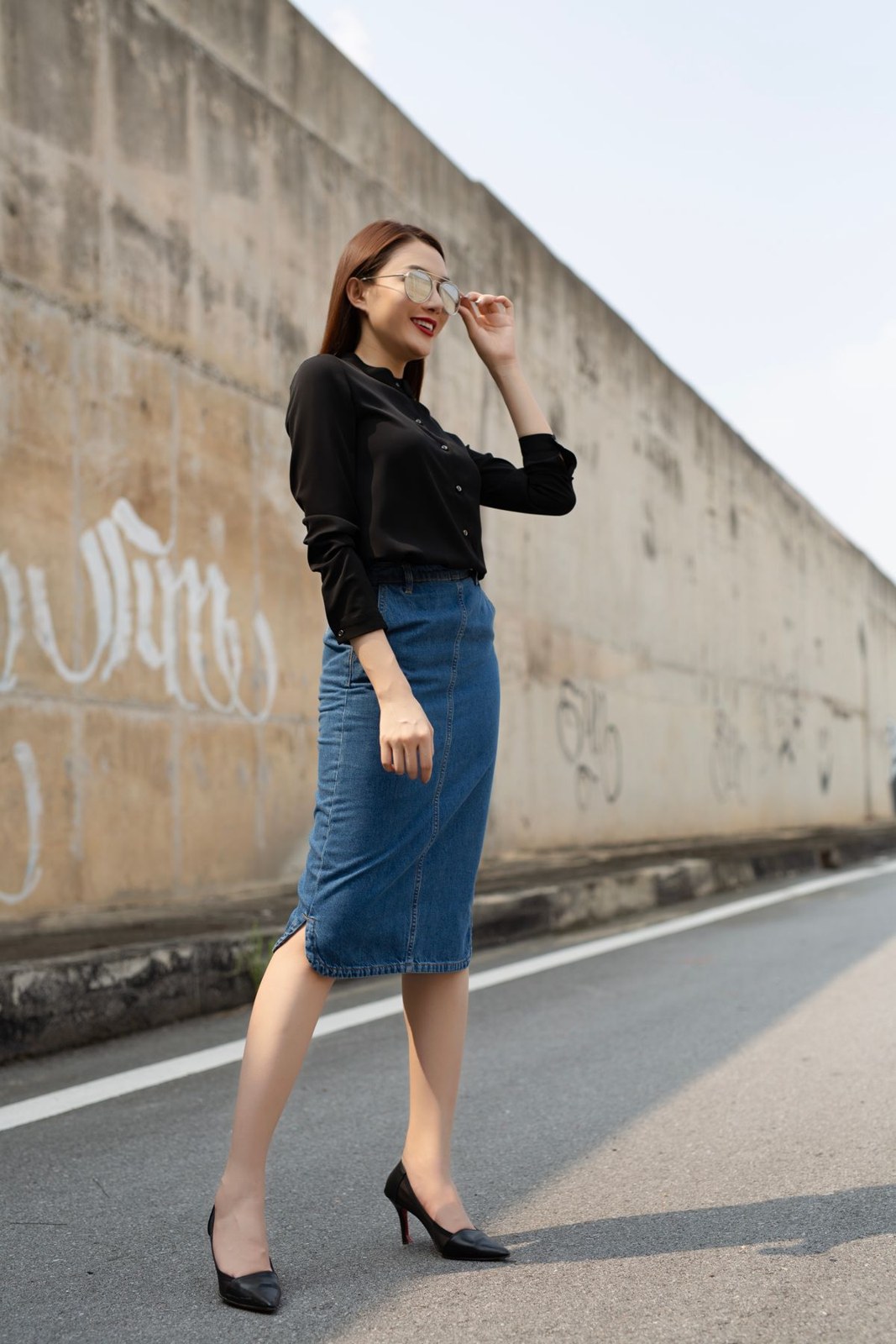 Black collared blouse, blue knee-length denim skirt, black pumps and sunglasses.