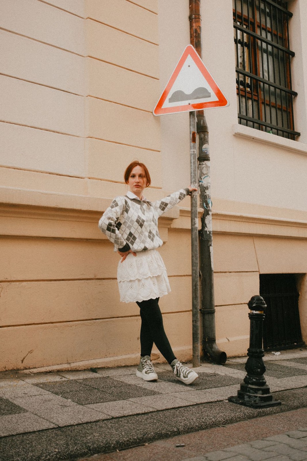 Grey diamond-pattern sweater, pale short skirt over black leggings and white trainers.