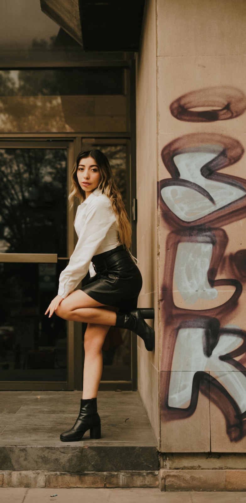 Light collared blouse, black miniskirt and black ankle boots beside a doorway.