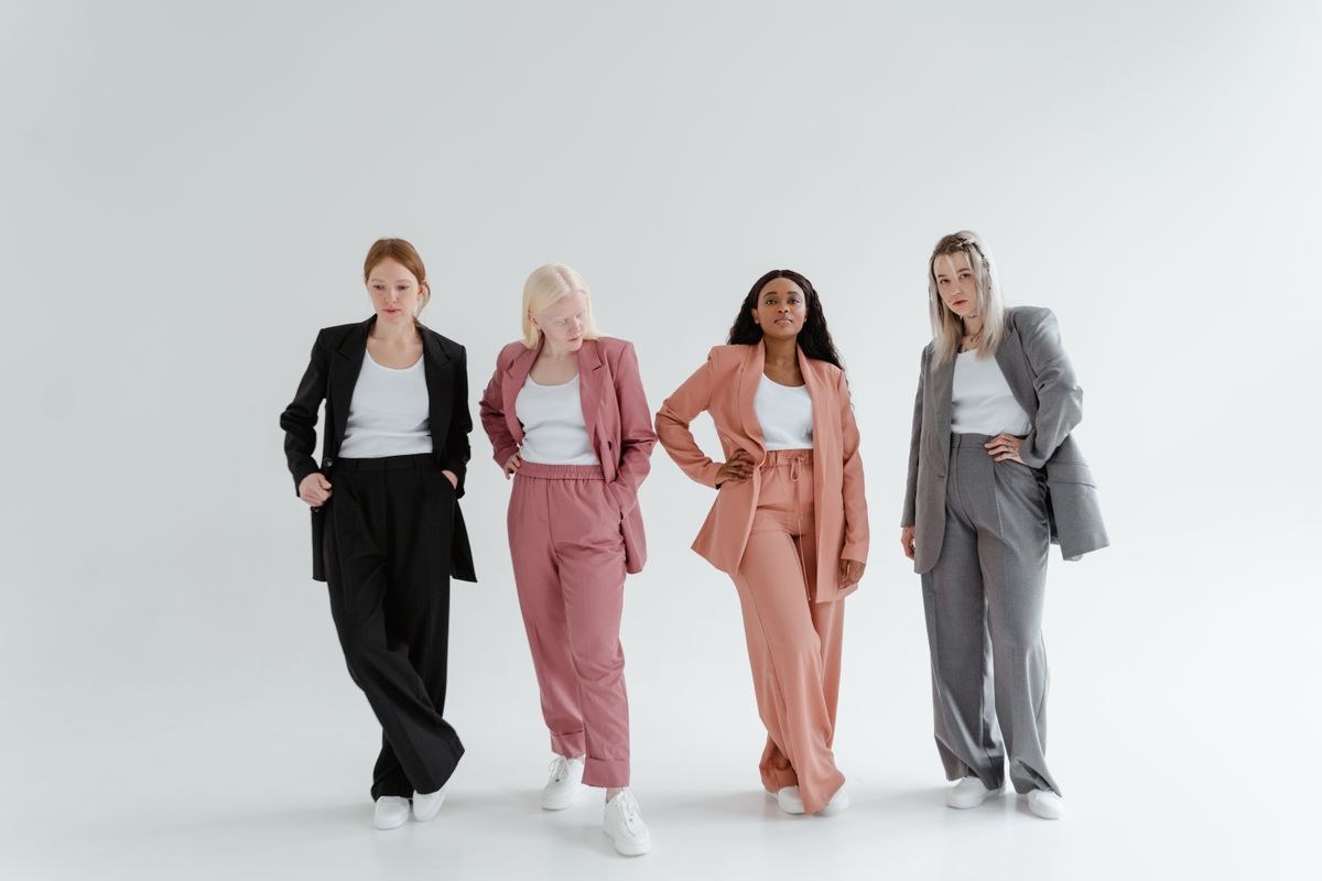 Four women in black, pink, coral and grey trouser suits with light tops and white trainers.