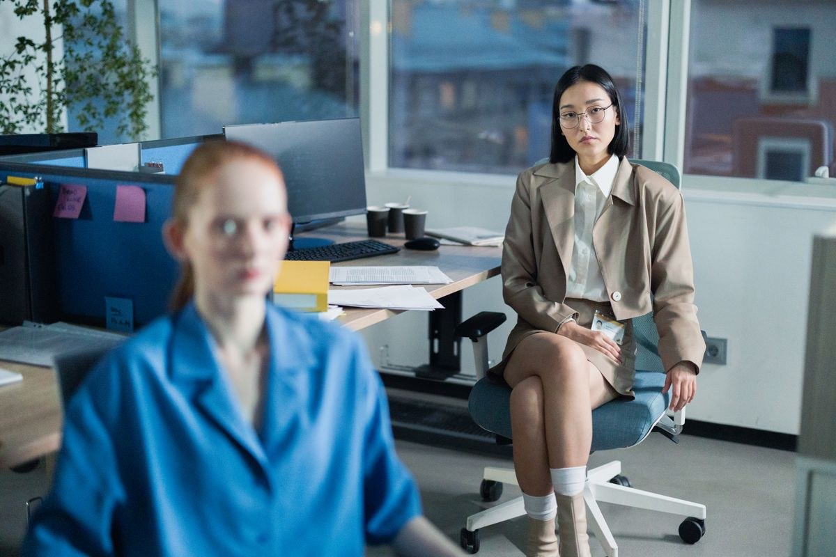 Seated woman in a tan belted blazer and matching shorts, white knee socks and trainers; blue blazer in foreground.