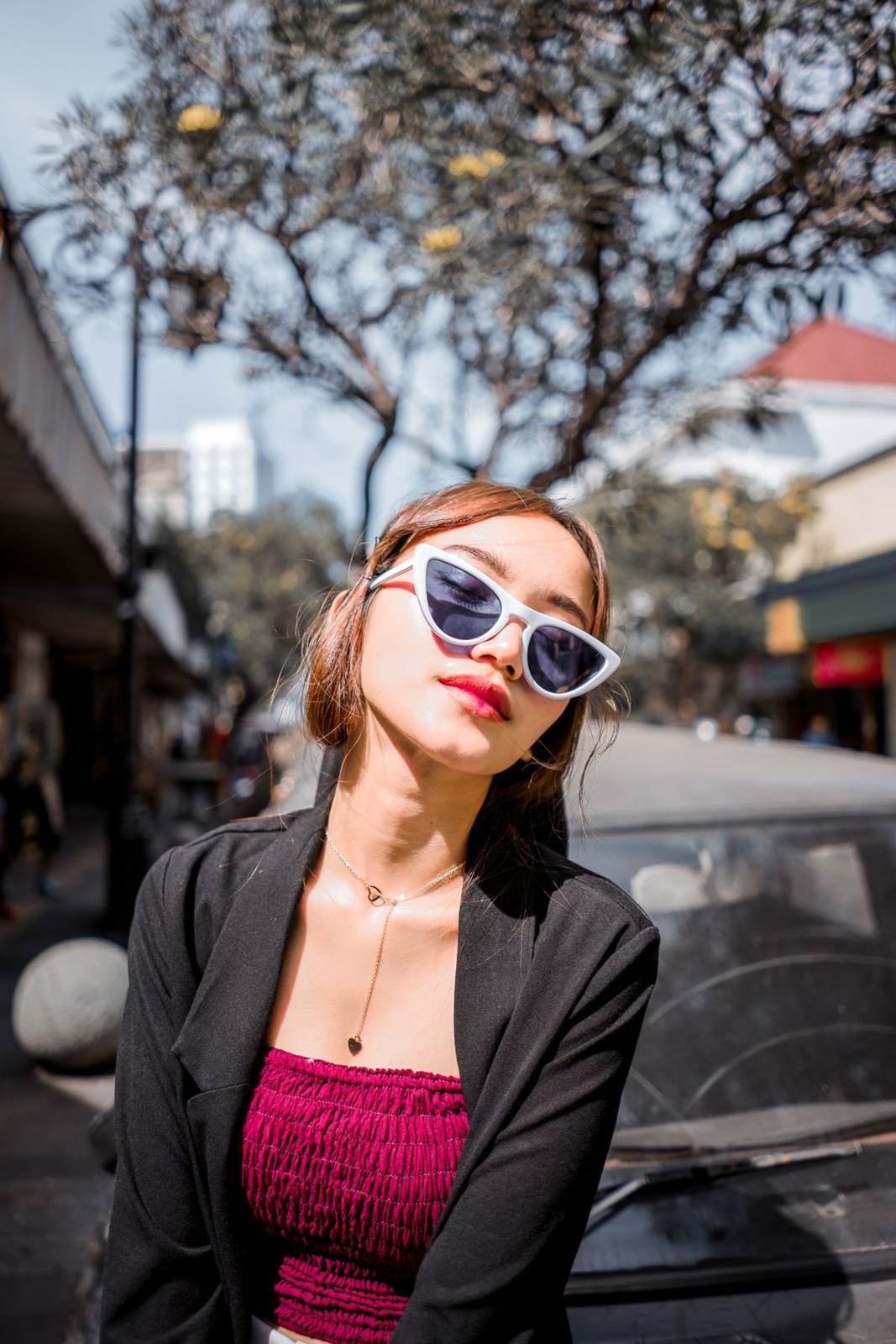 Black blazer over a textured burgundy top, with white sunglasses and a short necklace; upper-body crop.