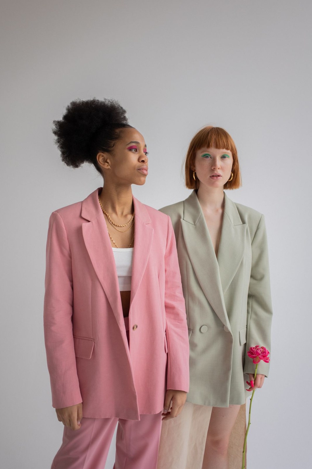 Two women: loose pink trouser suit with a light top and pale-grey short suit.