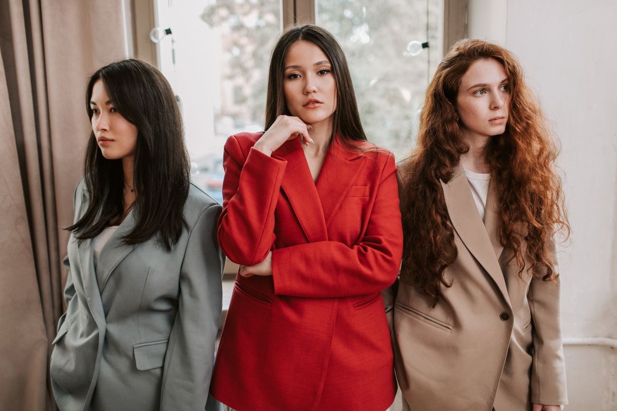 Three women in grey, red and tan blazers, cropped at the waist.