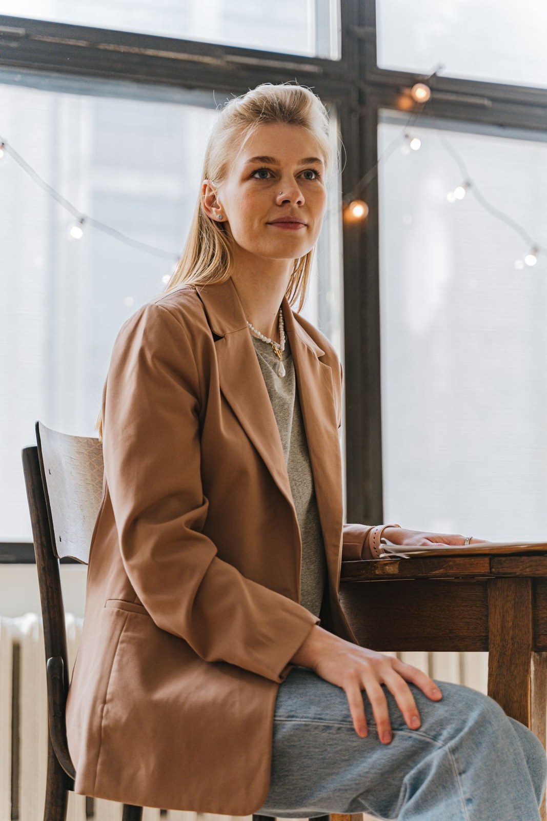 Tan blazer over a grey top with blue jeans, seated at a café.