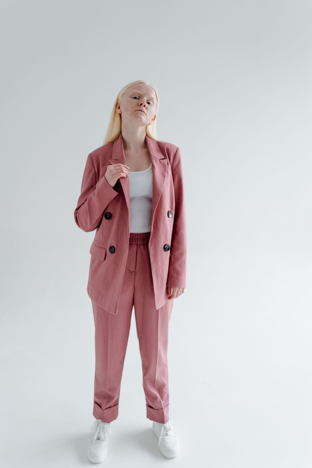 Pink trouser suit, white top and white trainers against a pale studio background.