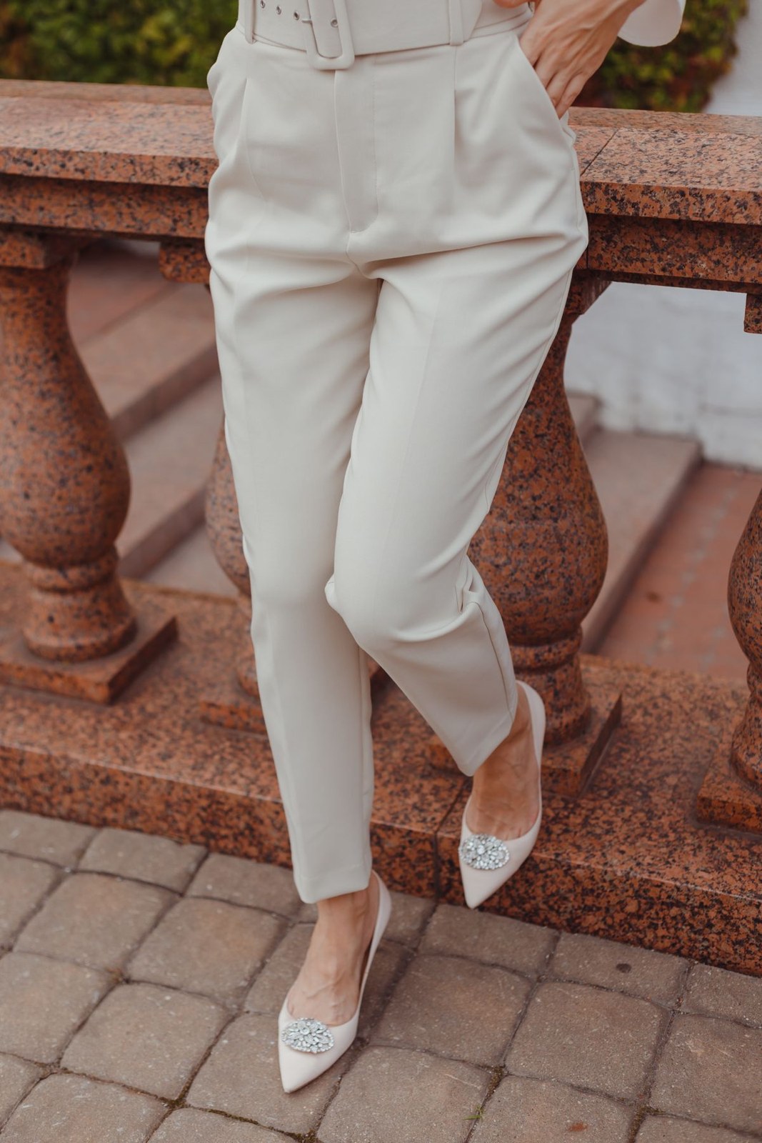 Cream high-waisted tailored trousers, matching belt and pale pointed shoes; lower-body detail.