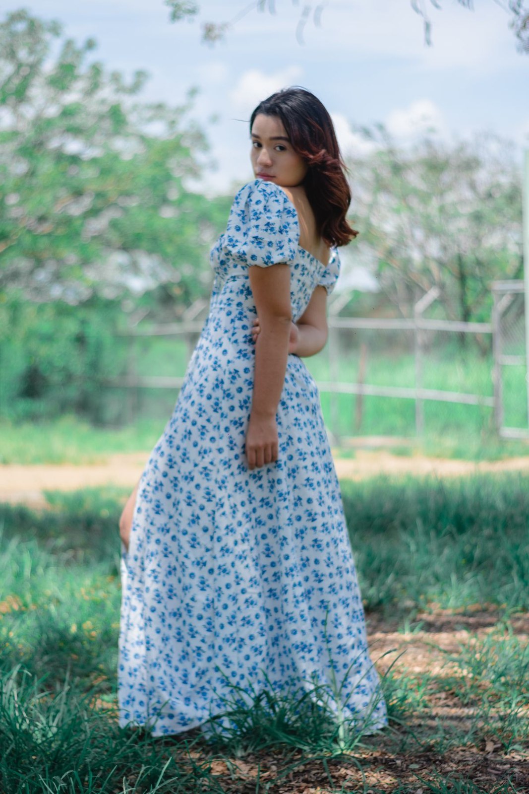 Langes hellblaues Blumenkleid mit kurzen Puffärmeln, betonter Taille und lockerem weitem Rock; der Saum verdeckt die Schuhe.