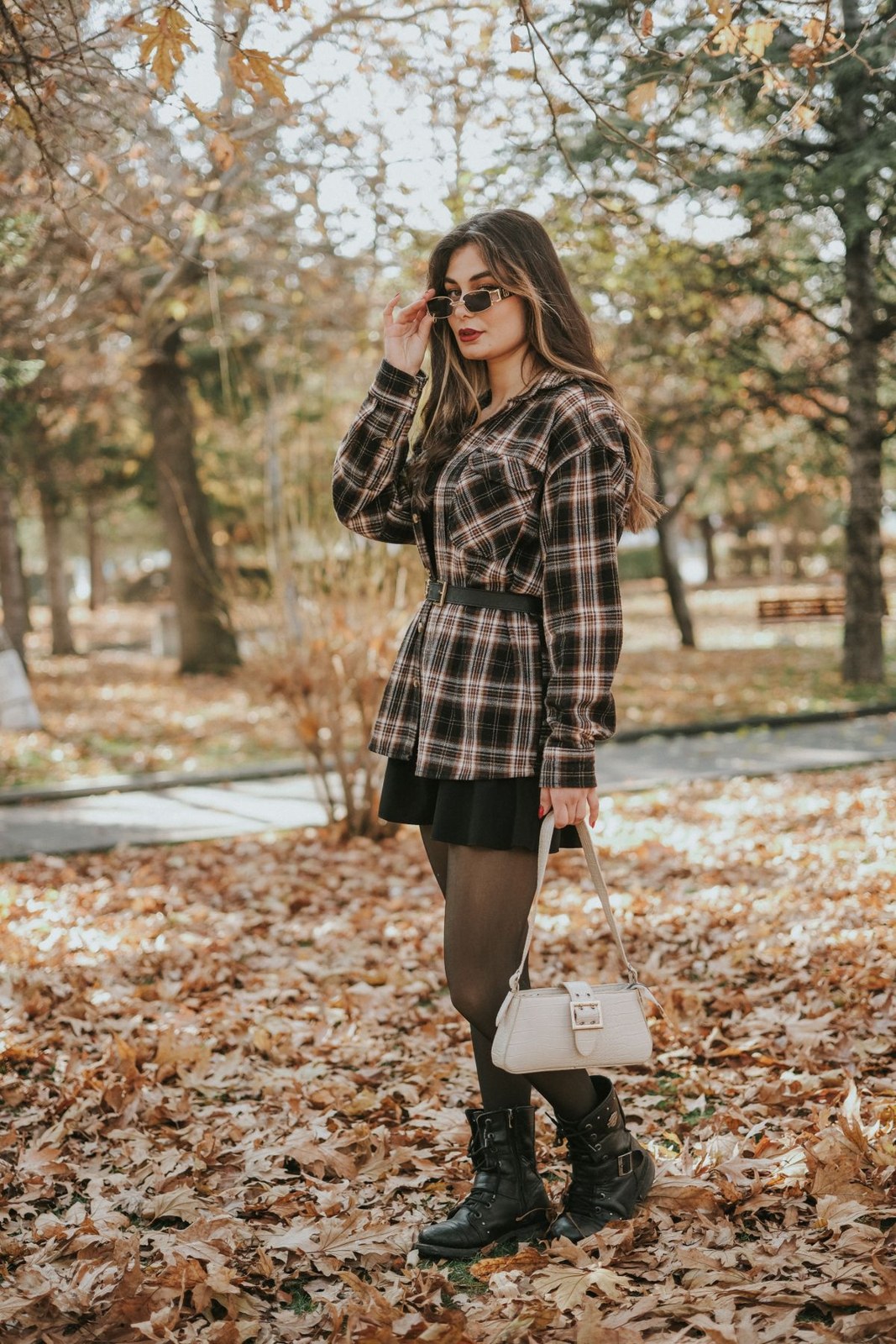 Short brown-grey checked coat over black miniskirt and tights, dark boots, beige handbag and sunglasses.