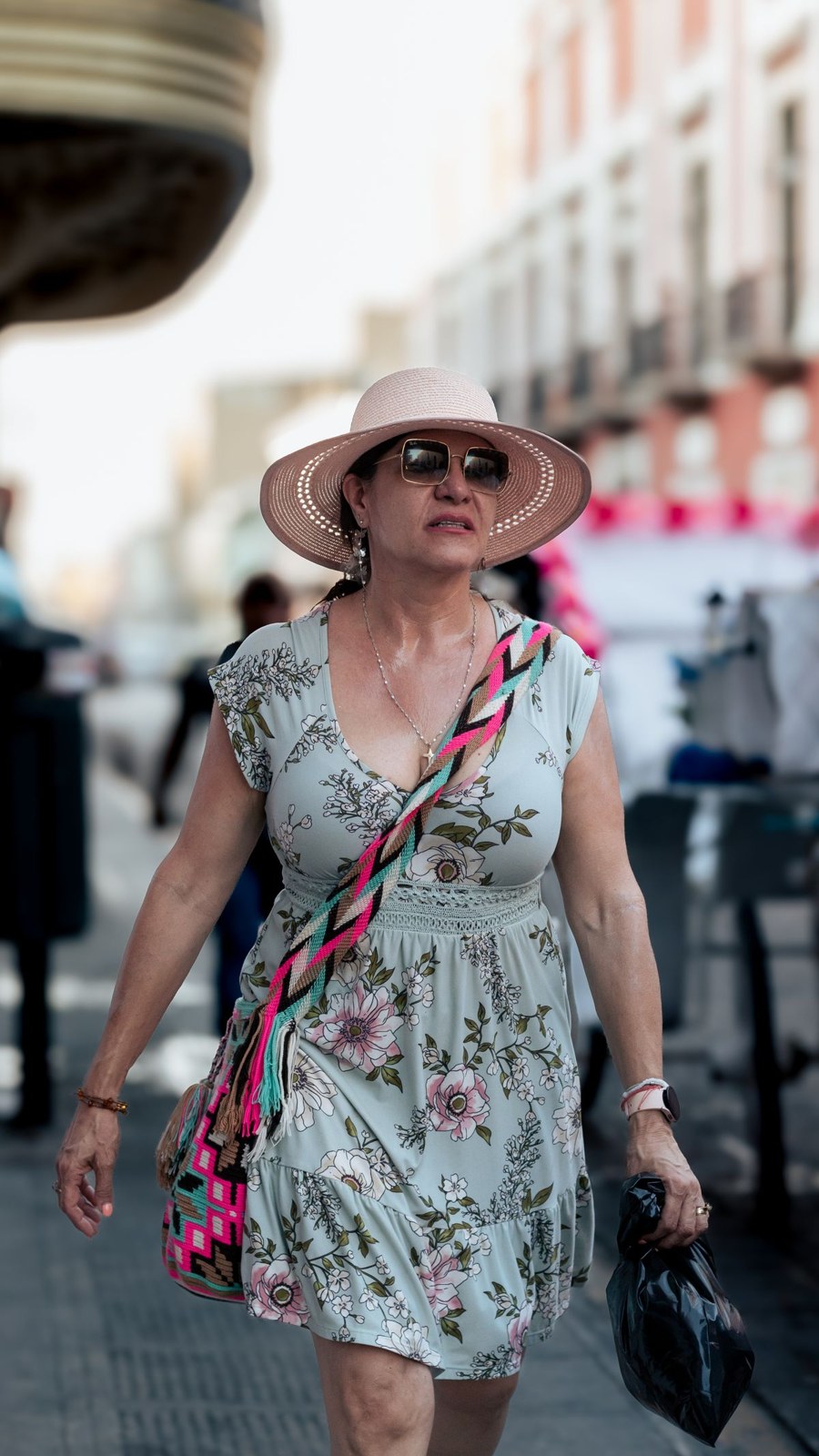 Light floral sleeveless dress, pale wide-brim hat, sunglasses and a colourful crossbody strap.