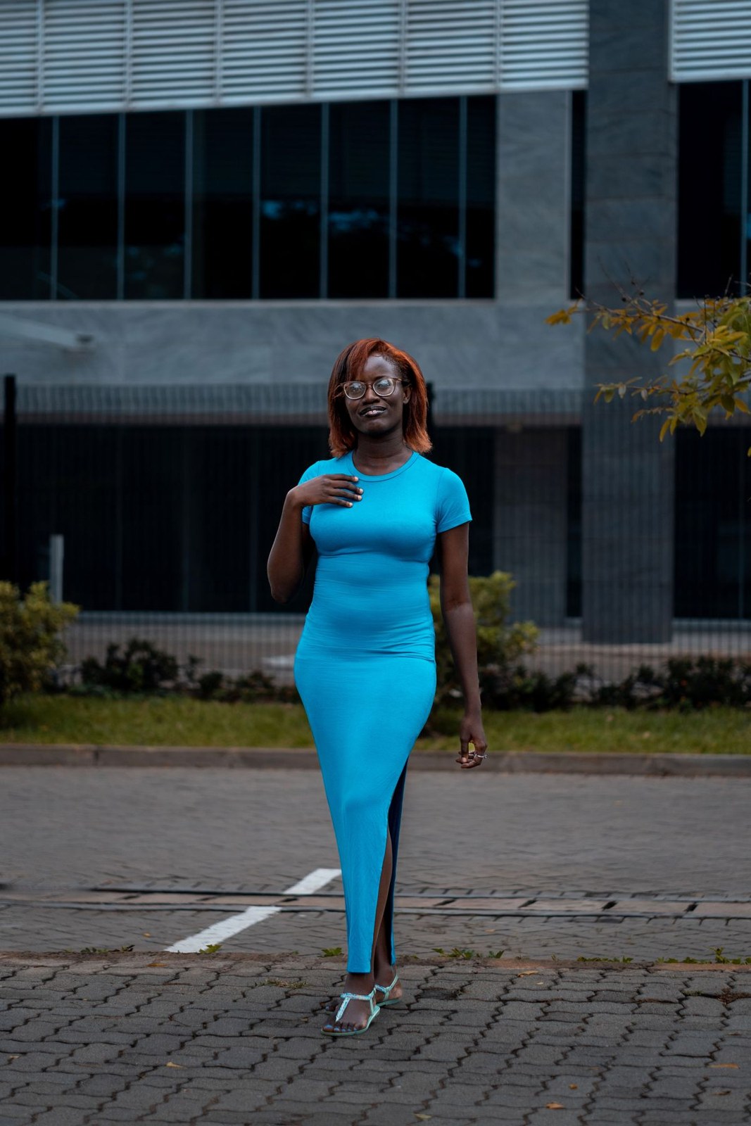 Bright turquoise fitted short-sleeve long dress with a slit, silver heels and a dark bag.