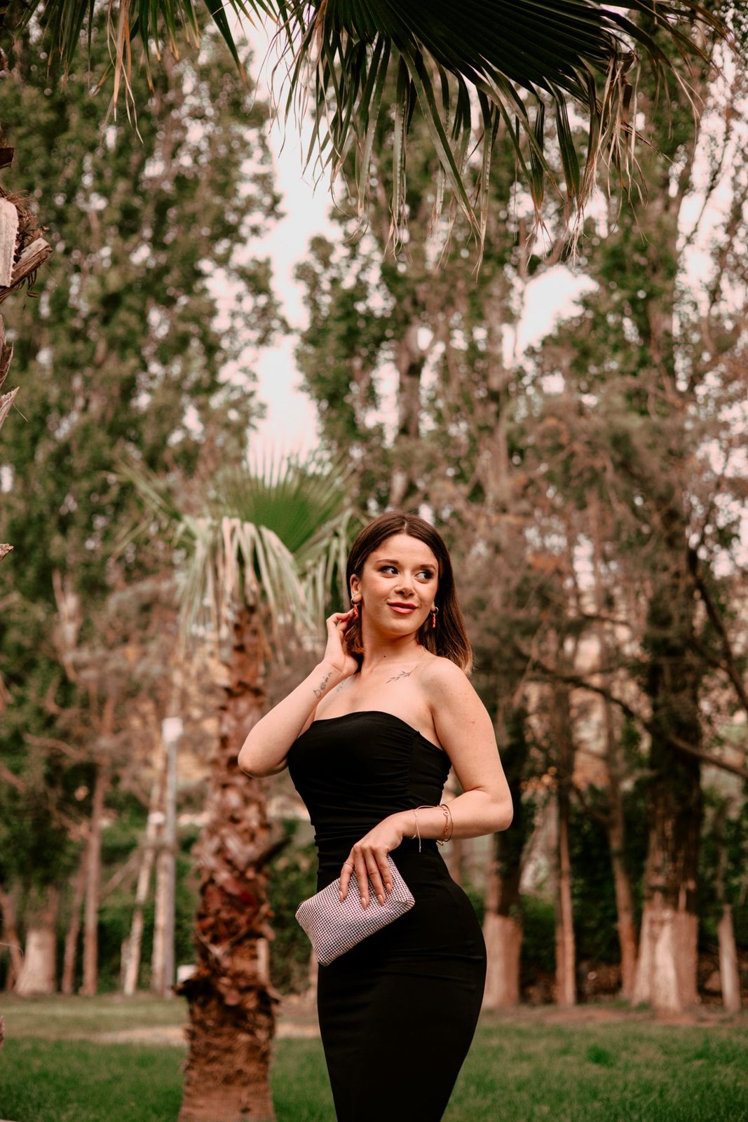 Black strapless long dress and a pale rectangular clutch outdoors.