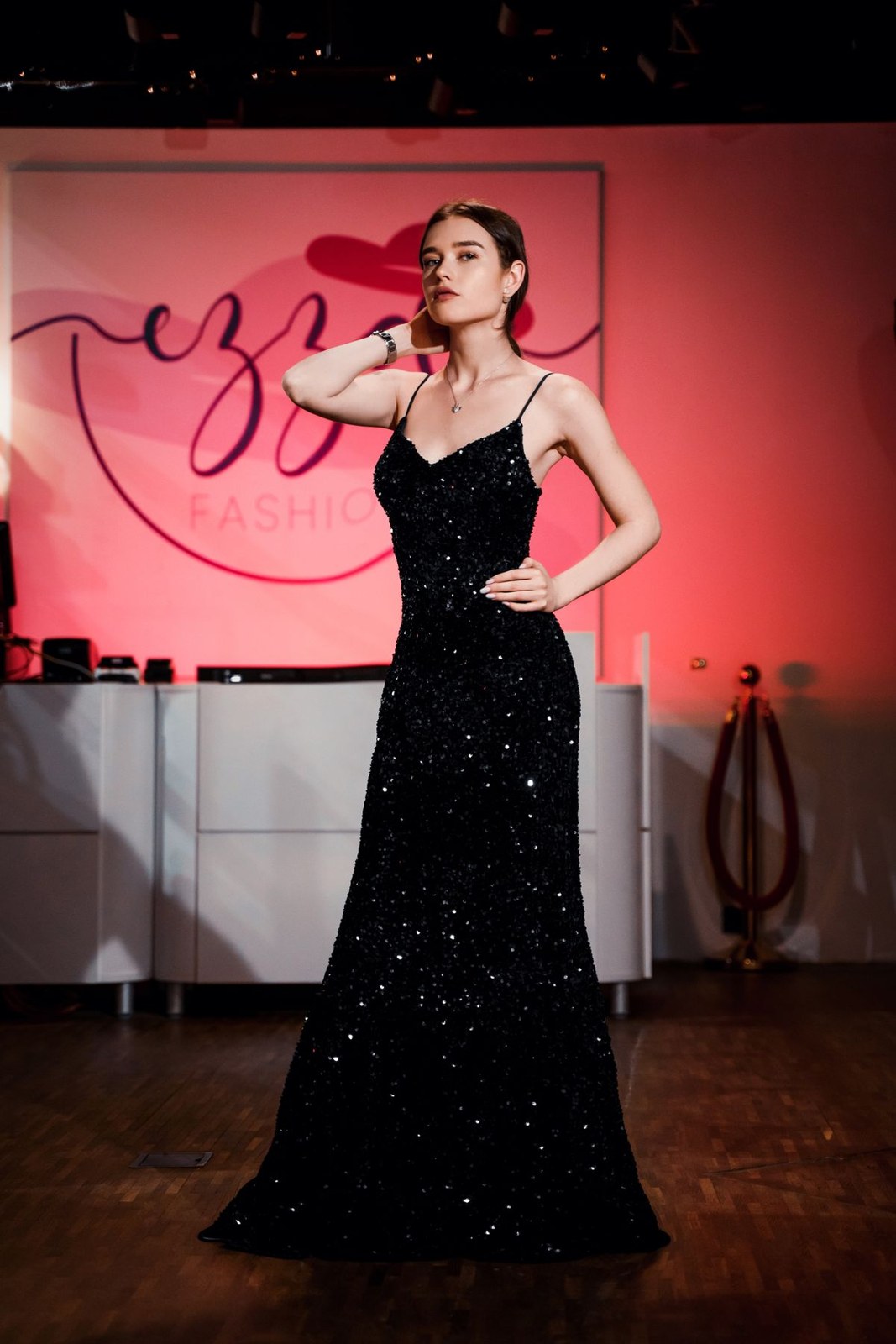 Long black sparkling fitted gown with thin straps and a flared hem indoors.