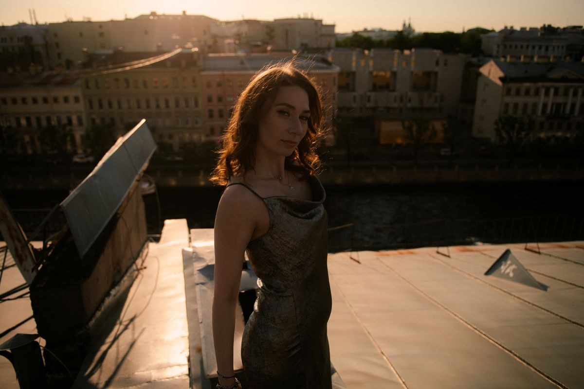 Dark sleeveless fitted long dress seen at sunset from the side.