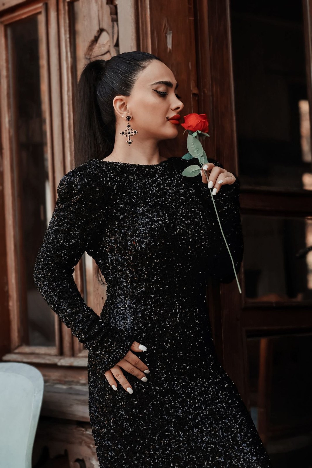 Black sparkling long-sleeve fitted dress with earrings in a portrait holding a red rose.