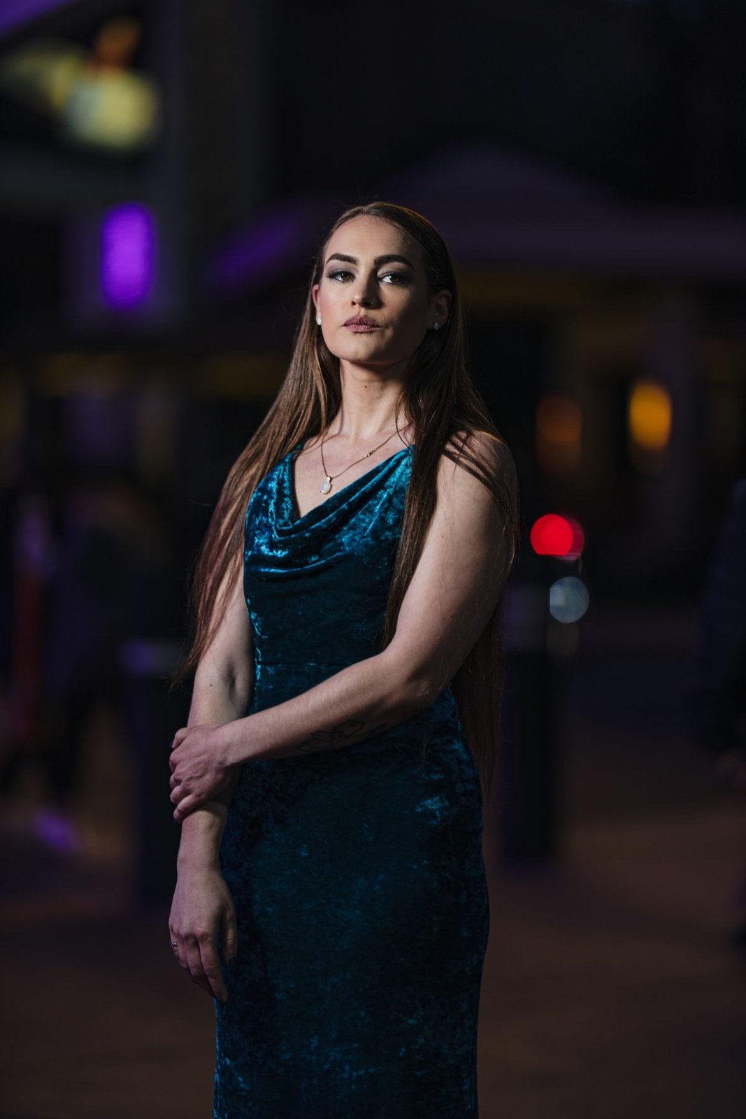 Dark teal draped sleeveless evening dress in an urban night portrait.