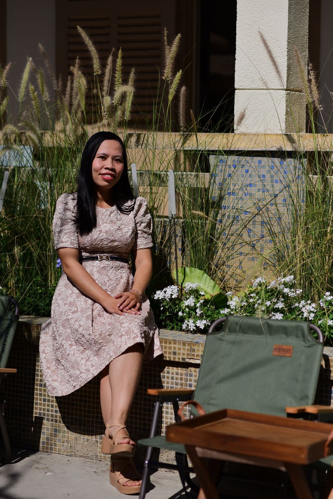 Pale small-print midi dress with a dark waist belt and dark open-toe shoes, seated outdoors.