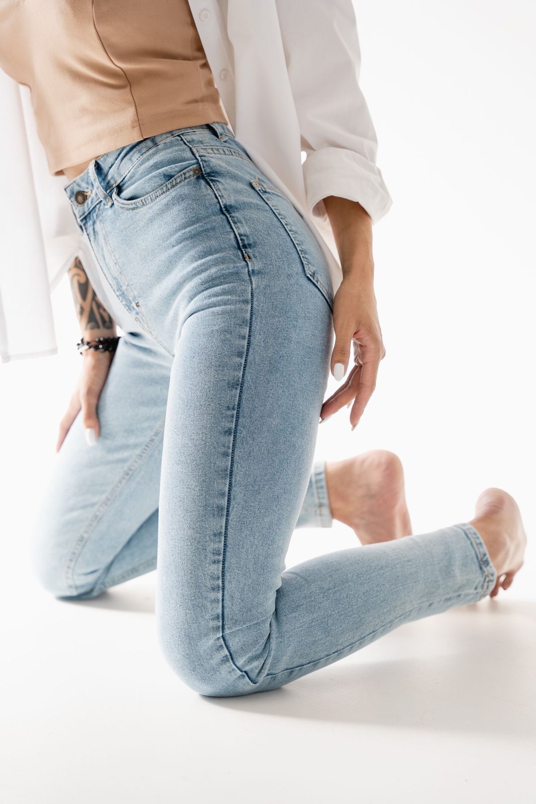 Open white shirt, beige fitted top and light slim jeans in a studio waist-to-knee crop.