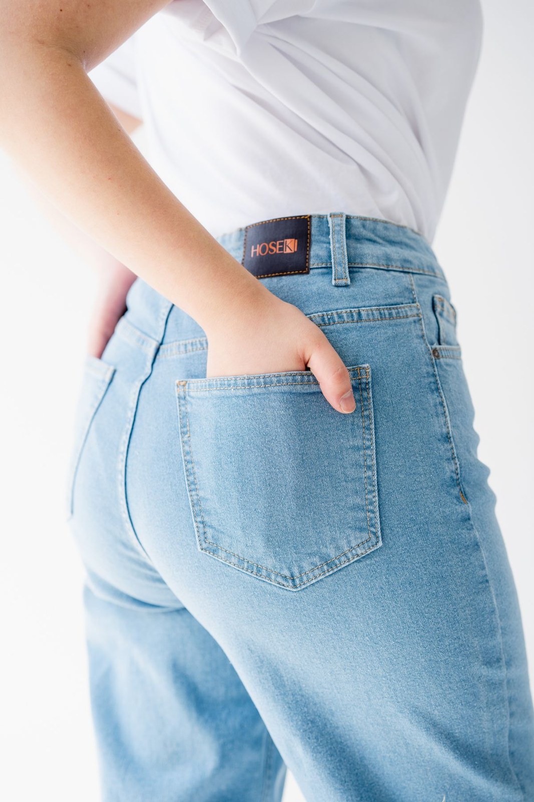 Gesäßtaschendetail einer hellblauen Jeans mit eingestecktem weißem Oberteil.