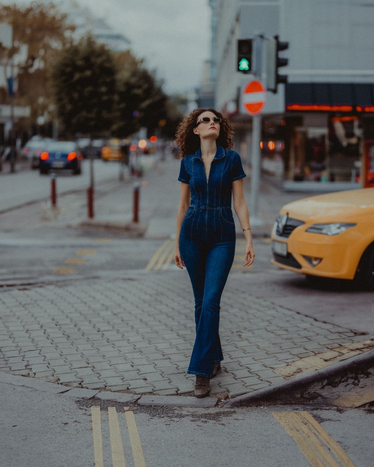 Dunkelblauer kurzärmeliger denimartiger Jumpsuit mit ausgestellten Beinen und hellbraunen Absatzschuhen auf einer Straße.