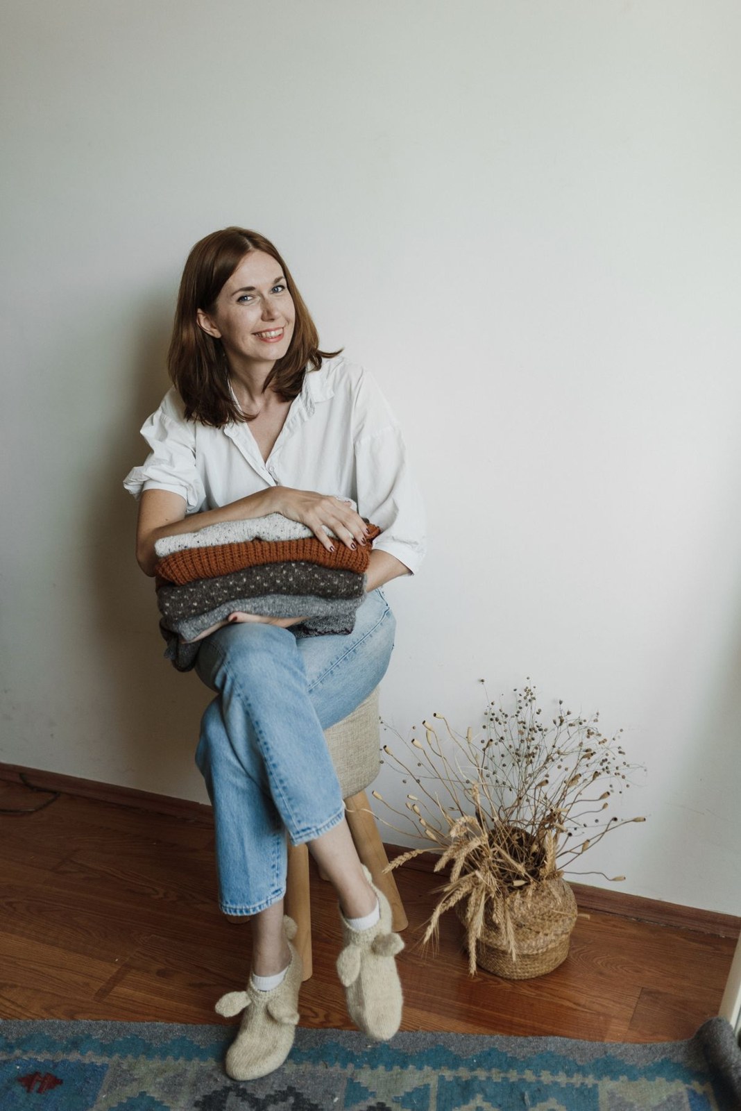 Weiße Hemdbluse, helle Jeans mit Umschlag und weiße Sneaker mit gefalteter neutraler Strickkleidung im Arm.