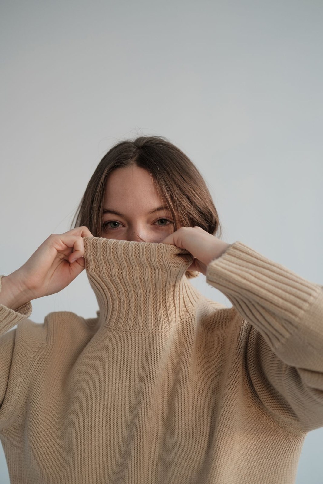 Beiger breit gerippter Rollkragenpullover im nahen Porträt, Kragen bis zum Gesicht gezogen.