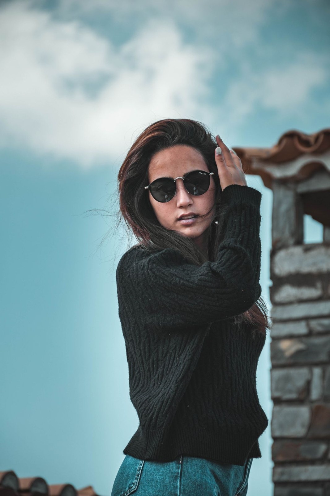 Schwarzer gerippter Rollkragenpullover, blaue Jeans und runde Sonnenbrille im Oberkörperausschnitt draußen.