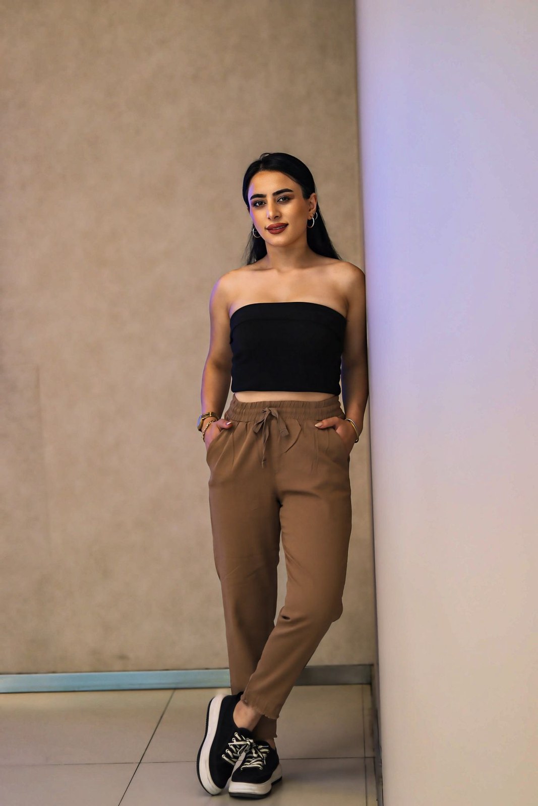 Schwarzes trägerloses Crop-Top, hellbraune schmal zulaufende Hose und schwarz-weiße Sneaker.