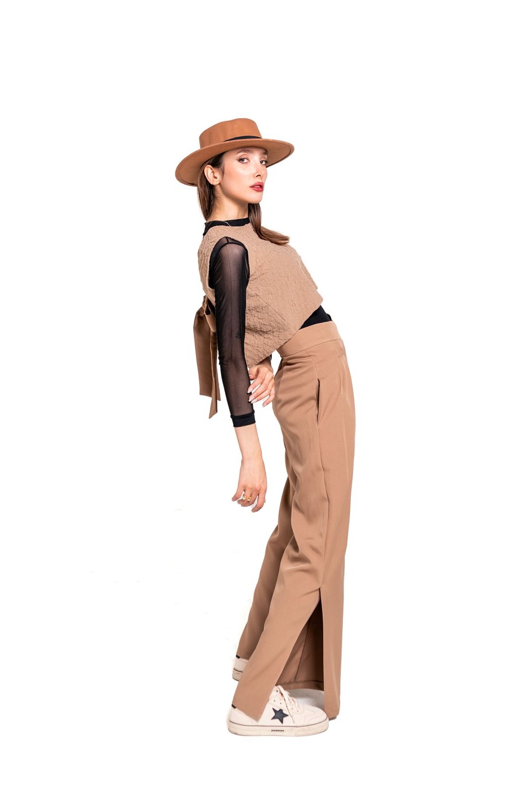 Hellbraune ärmellose Weste und passende weite Hose mit schwarzem Top, braunem Hut und weißen Sneakern.